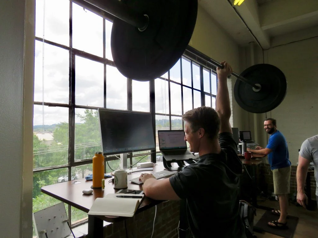 Man working on a laptop while lifting a weight with one hand