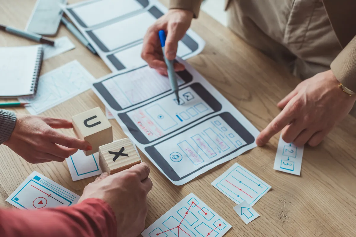 designers with mobile website schematics, sketches and ux letter cubes on the table