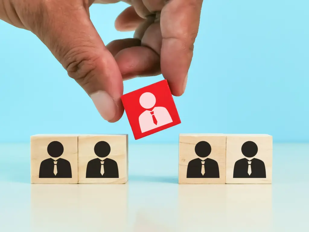 Hand picking a red block with a white figure, highlighting a specific employee or resource for IT staff augmentation or hiring.