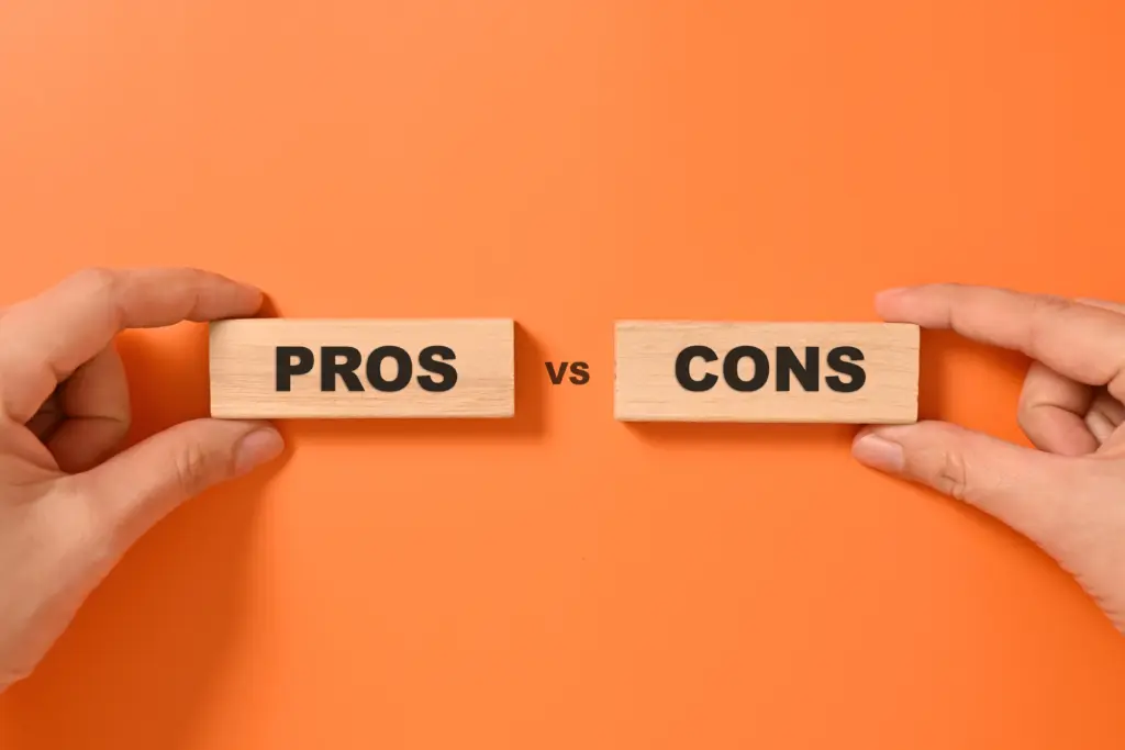 Hands holding wooden blocks with the words "PROS" and "CONS" separated by "vs" on a vibrant orange background.