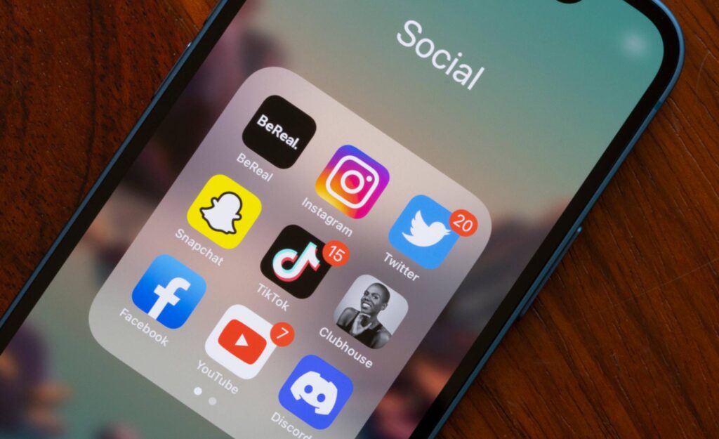 A smartphone screen displaying social media apps, including Instagram, Twitter, TikTok, Snapchat, Facebook, YouTube, and Discord, with notification badges.