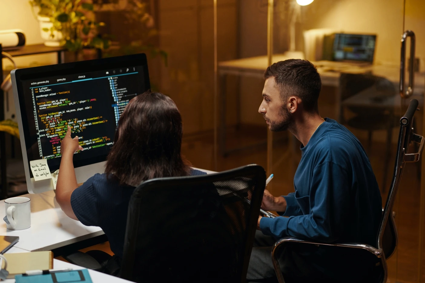 Two software engineers reviewing source code on a large monitor and pointing out bugs during a QA session.
