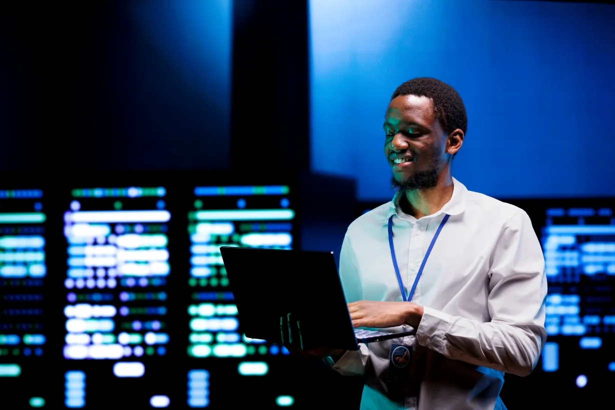 A unosquare engineer holding a laptop in a server room, managing the Harvard Business Publishing cloud migration to AWS.
