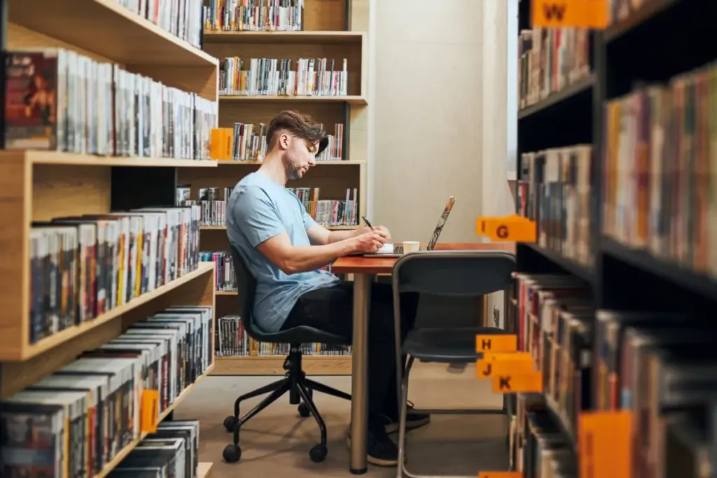 A professional working on a laptop and taking notes in a media archive room, representing unosquare's digital engineering solutions for the media and publishing industry.