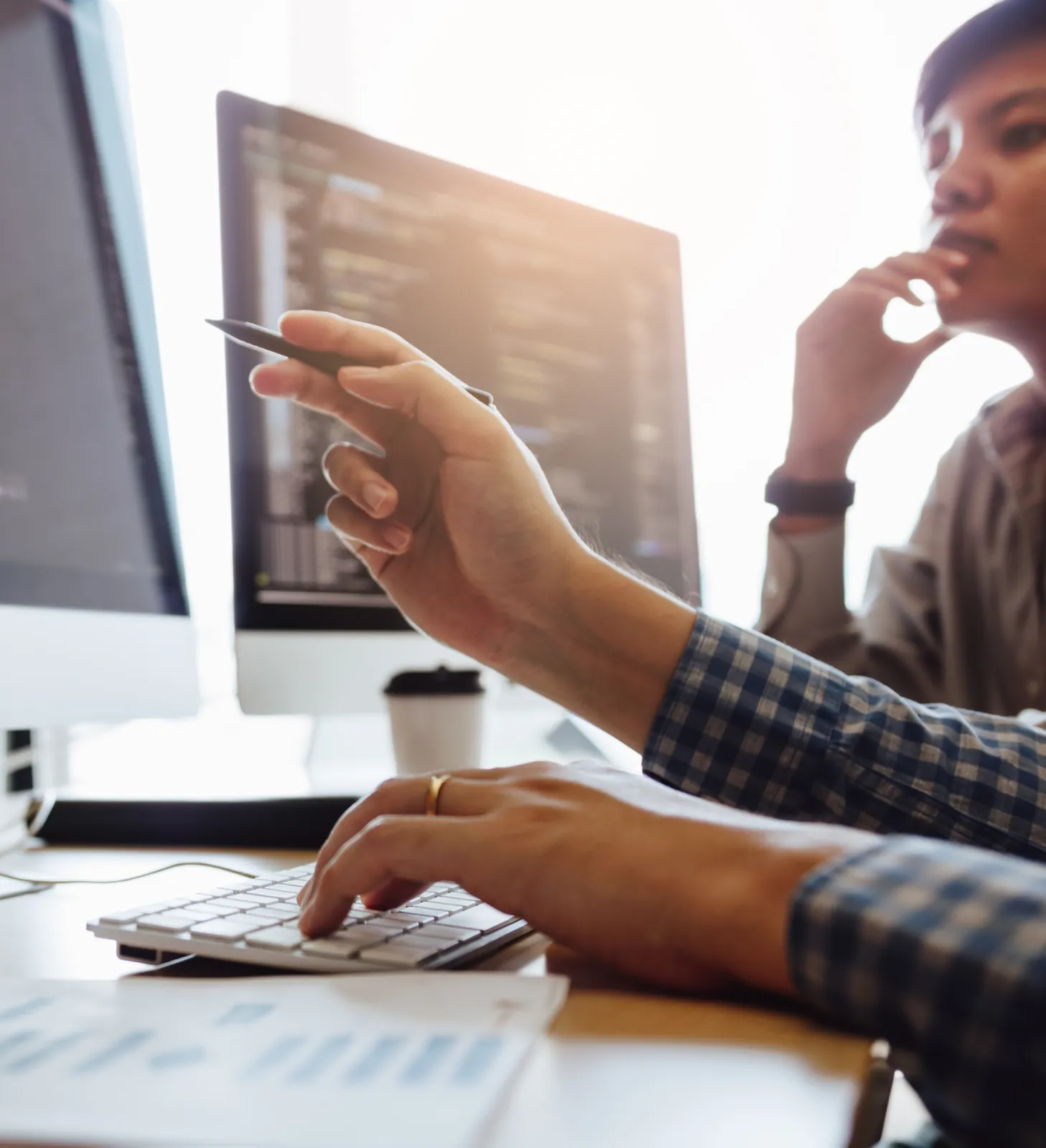 An engineer points at code on a monitor while a colleague reviews it